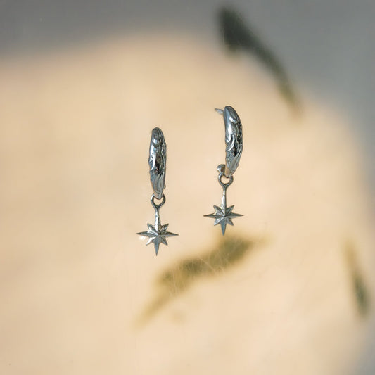 Sterling silver hoop earrings with eight pointed star-shaped charms on a blurred background
